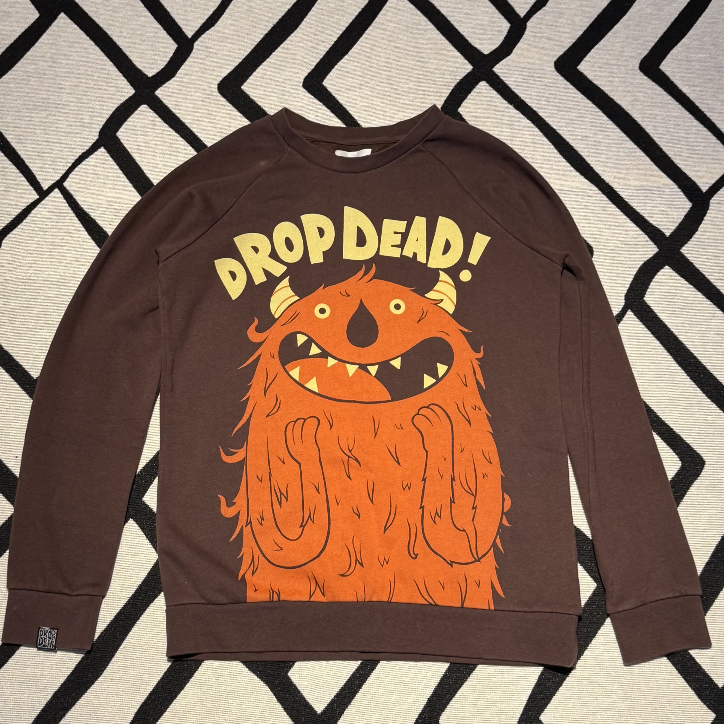 frente do moletom marrom Drop Dead com monstro laranja